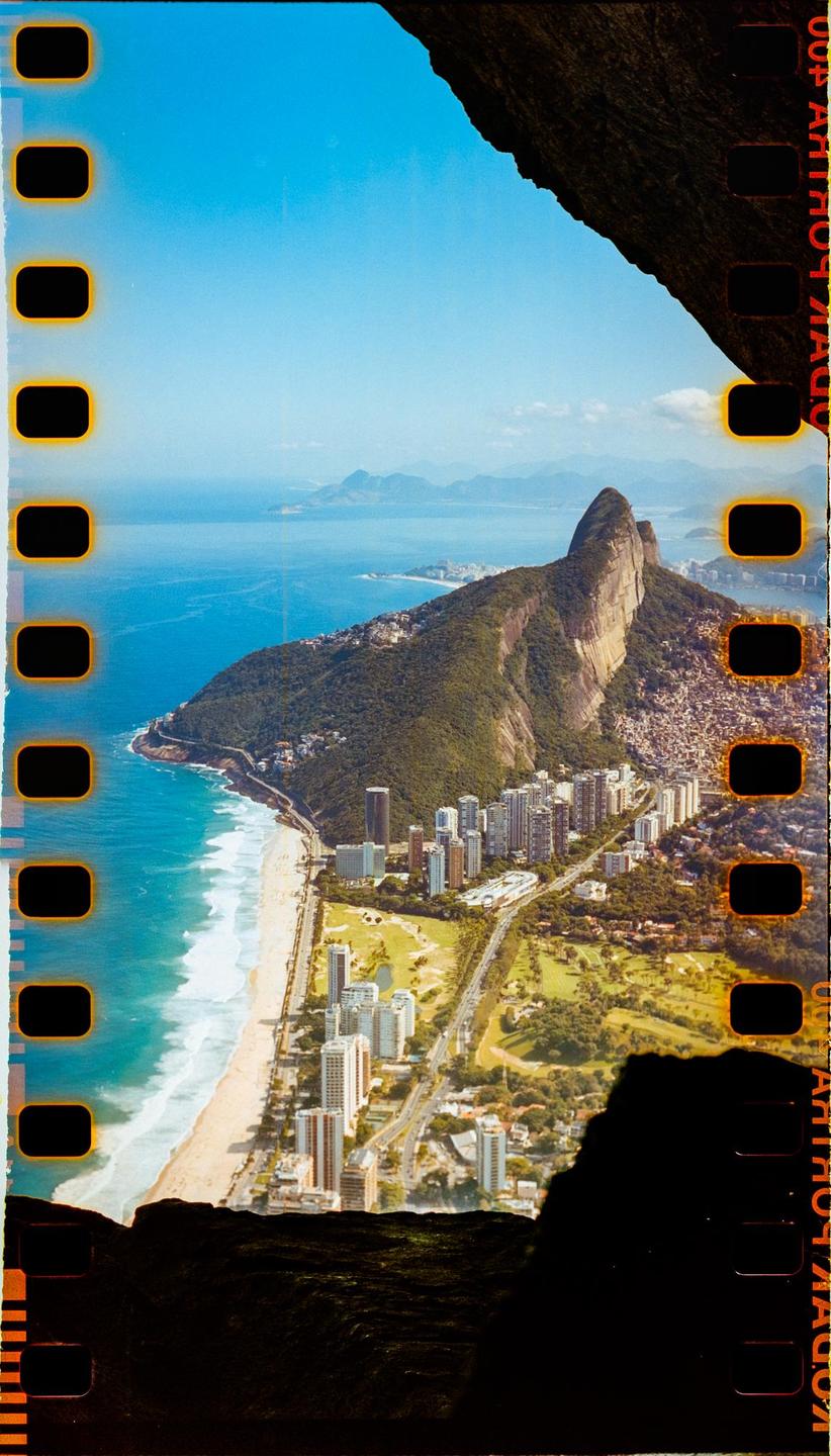 An aerial view shows a city with a beach, ocean, and a large mountain.