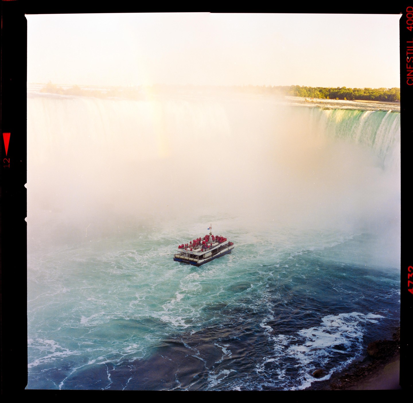 A boat full of people floats on the water near Niagara Falls, which is shrouded in mist.