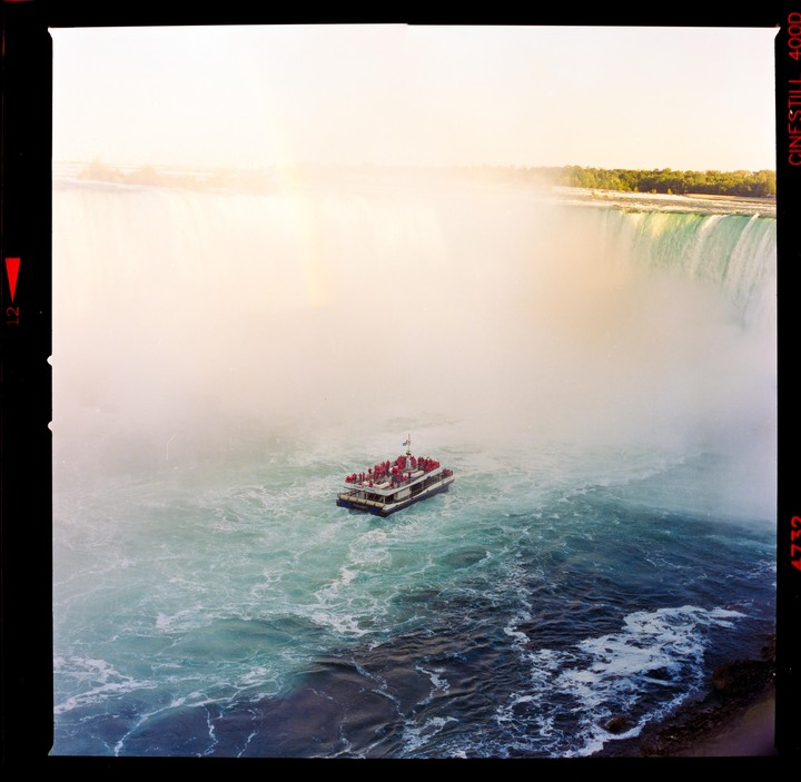 A boat full of people floats on the water near Niagara Falls, which is shrouded in mist.