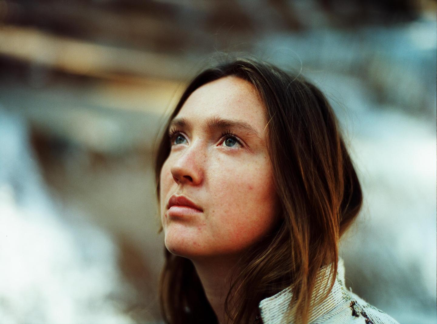 A woman with long hair and freckles looks up and to the left.