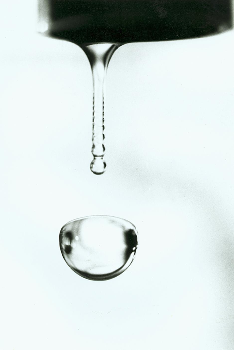 A stream of water drips from a faucet, forming a large bubble below.