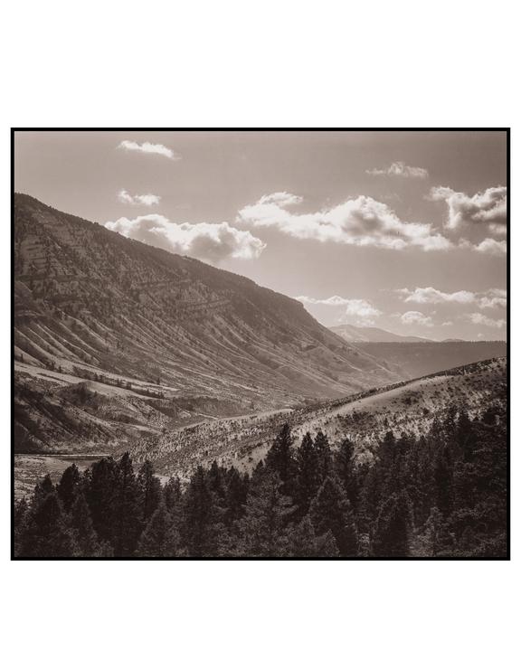 A sepia-toned landscape shows a valley with mountains, hills, and a forest under a cloudy sky.