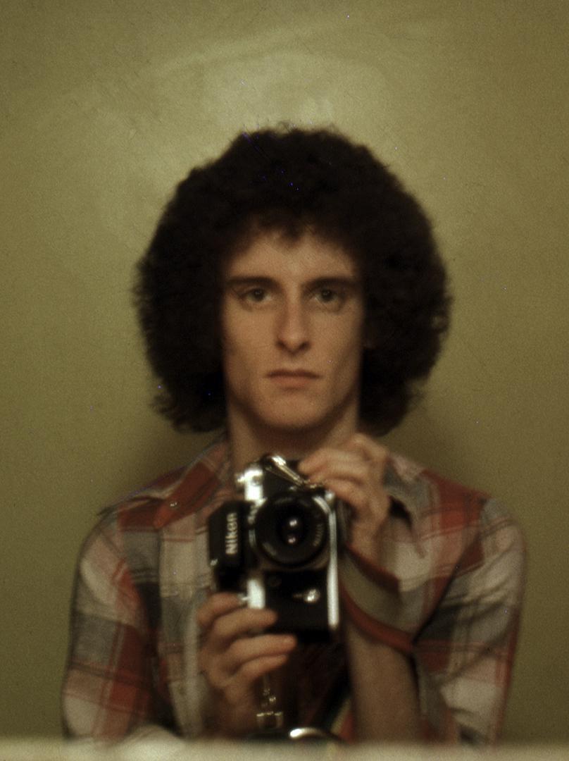 A man with an afro hairstyle holds a camera in a self-portrait.