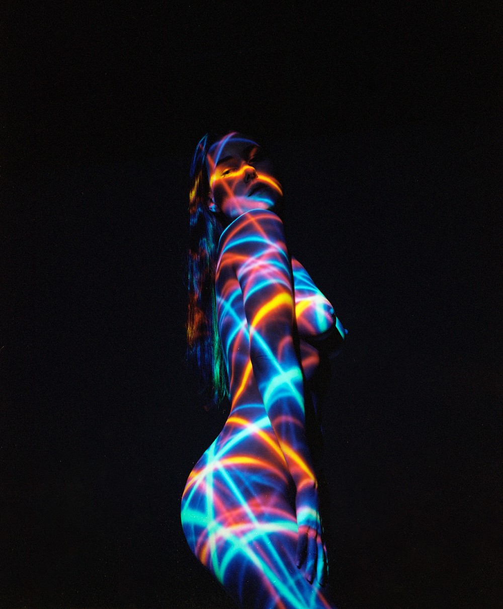 A woman is illuminated by colorful laser light patterns on a dark background.