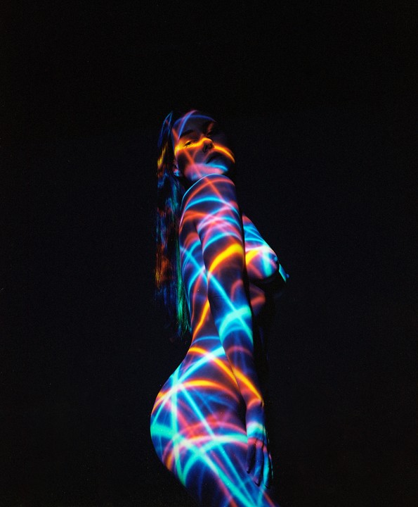 A woman is illuminated by colorful laser light patterns on a dark background.
