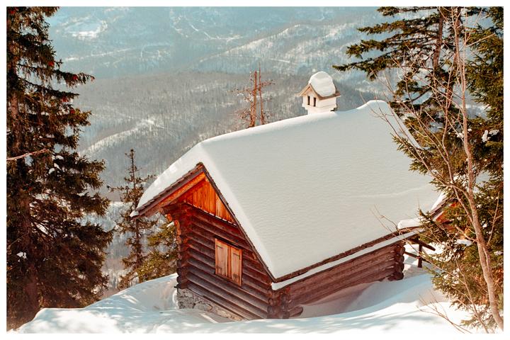 A wooden cabin with a snow-covered roof is nestled among pine trees on a snowy mountain.