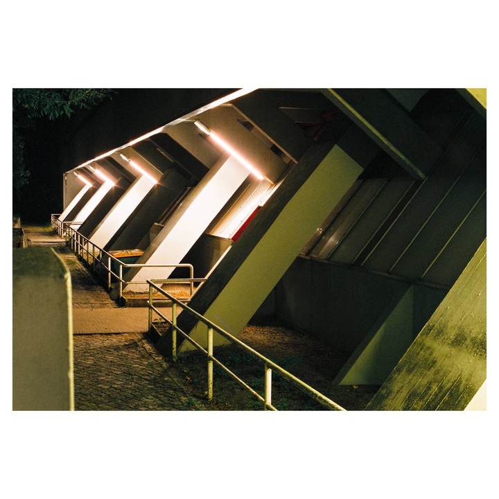 A series of illuminated concrete structures with railings line a path at night.