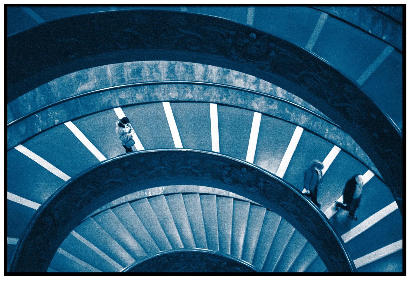 Three people walk down a spiral staircase with white stripes on the steps.