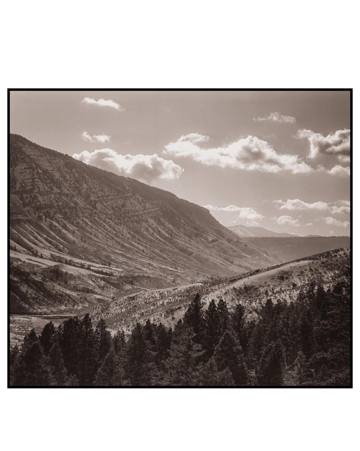 A sepia-toned landscape shows a valley with mountains, hills, and a forest under a cloudy sky.