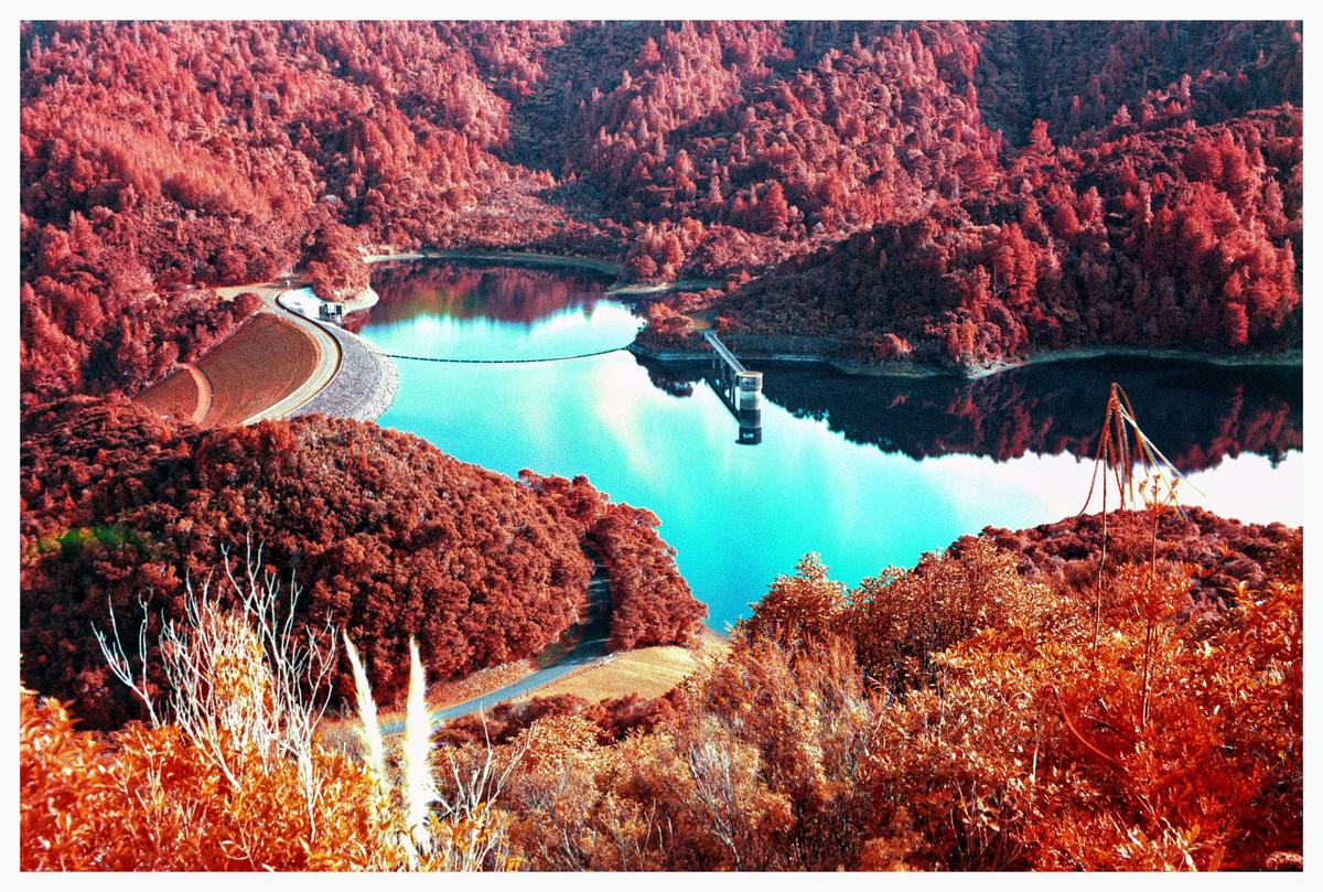 A body of water is surrounded by red foliage and a dam, with a structure extending into the water.