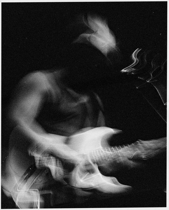 A blurry figure plays an electric guitar in a dark setting.