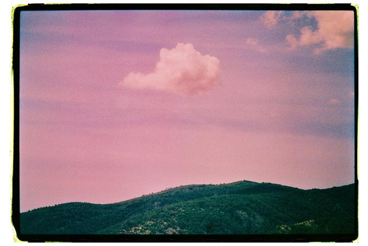 A single cloud floats in a pink sky above a green mountain.