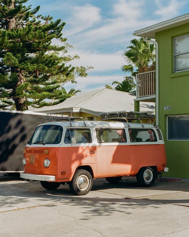 An orange and white van is parked on a concrete surface next to a green building.