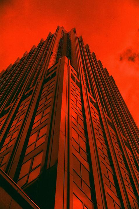 A tall building with many windows is photographed from below against a red sky.