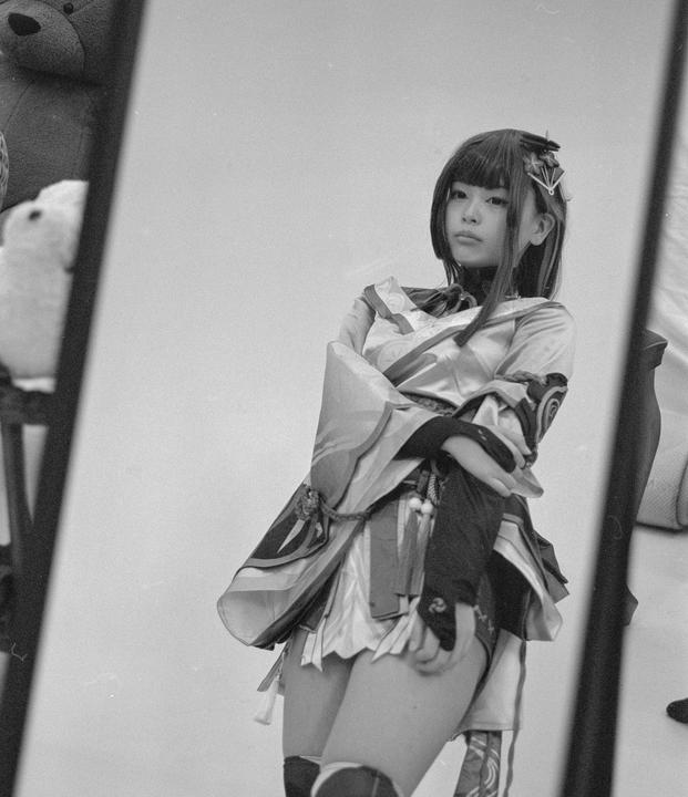 A young woman in costume is reflected in a mirror, with a teddy bear visible in the background.