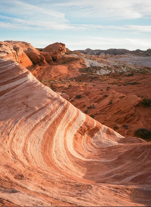 A landscape view shows red and white striped rock formations under a blue sky with clouds.
