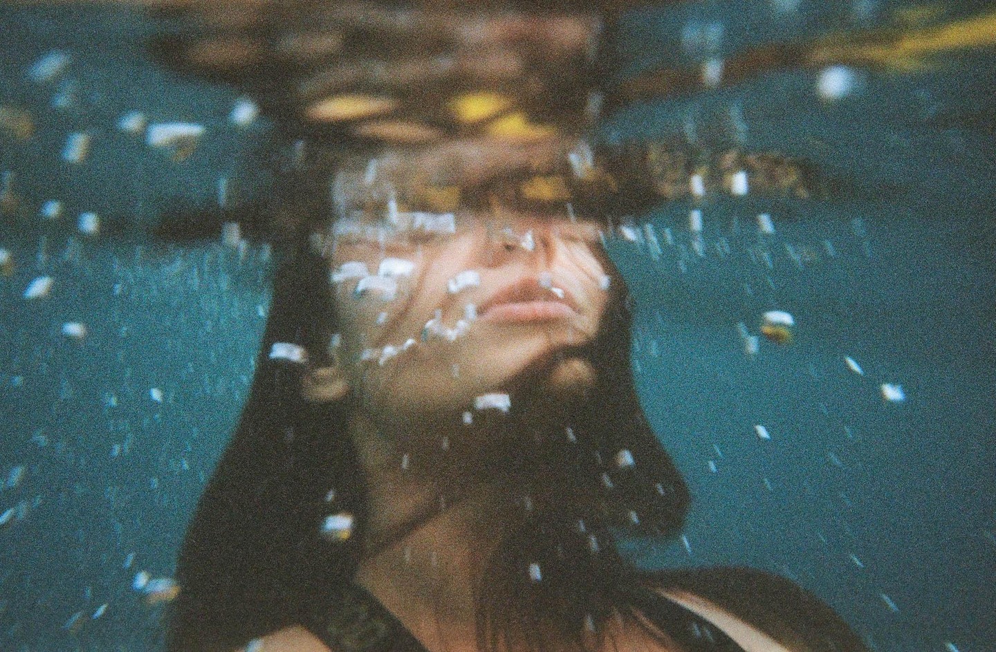 A woman's face is visible underwater, surrounded by bubbles.