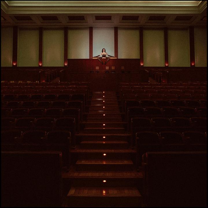 A woman sits on a ledge above rows of empty seats in a cinema.