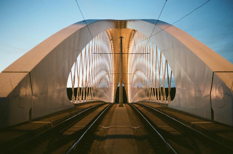 A tram bridge with illuminated arches stretches into the distance under a clear sky.
