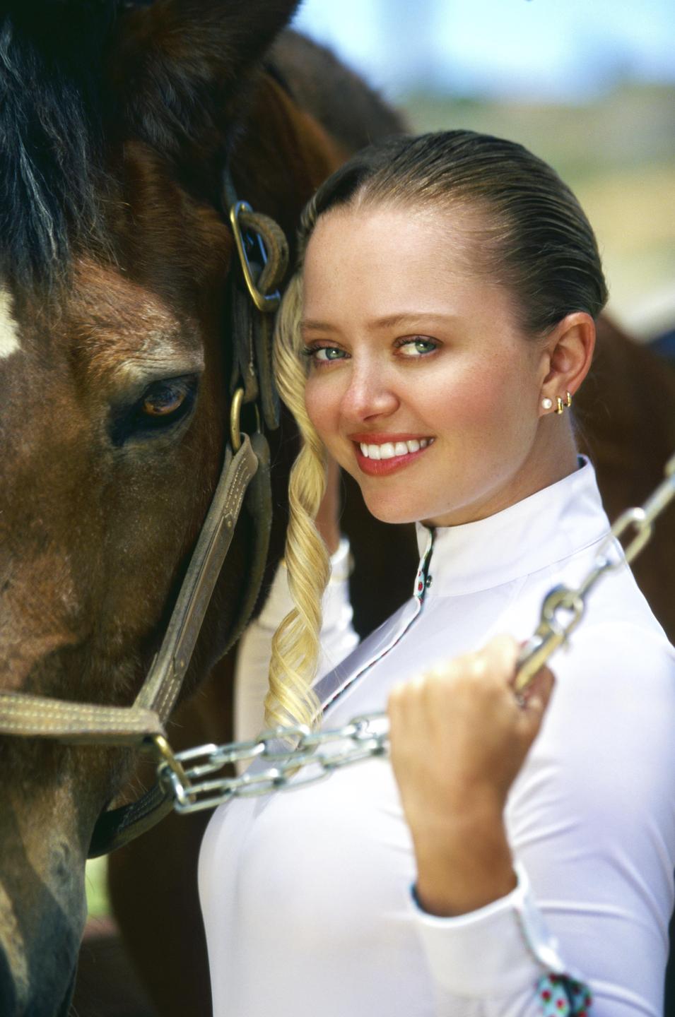 A woman in a white shirt holds a chain next to a horse.