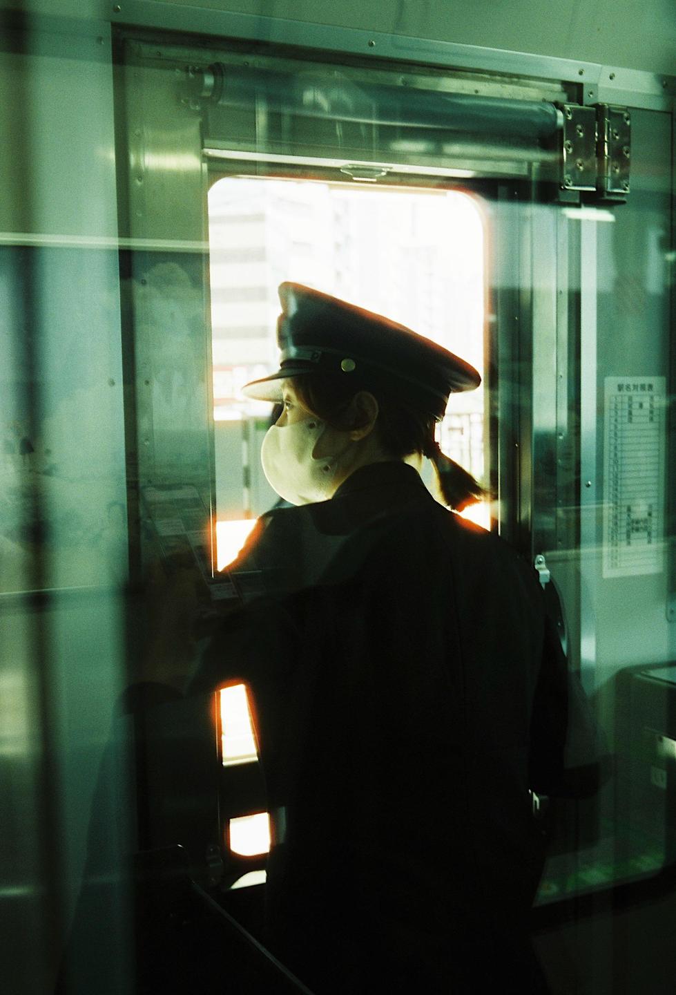A person in a uniform and a face mask looks out a train window.