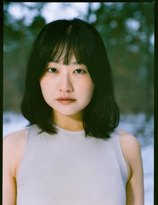 A woman with dark hair and bangs looks directly at the viewer.