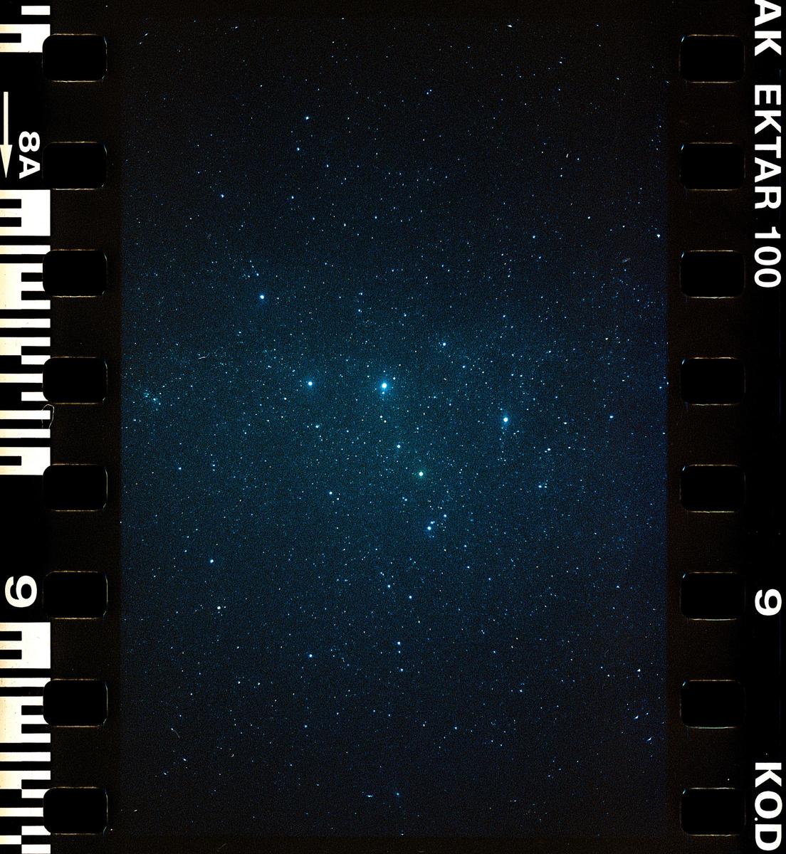 A dark night sky is filled with numerous bright stars, with a cluster of prominent stars visible in the center.