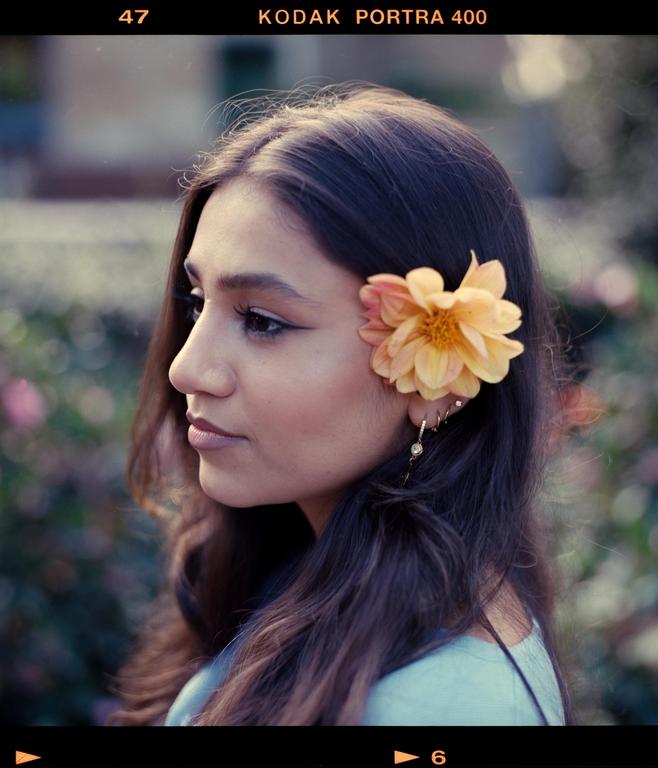 A woman with long hair and a flower tucked behind her ear looks to the left of the frame.