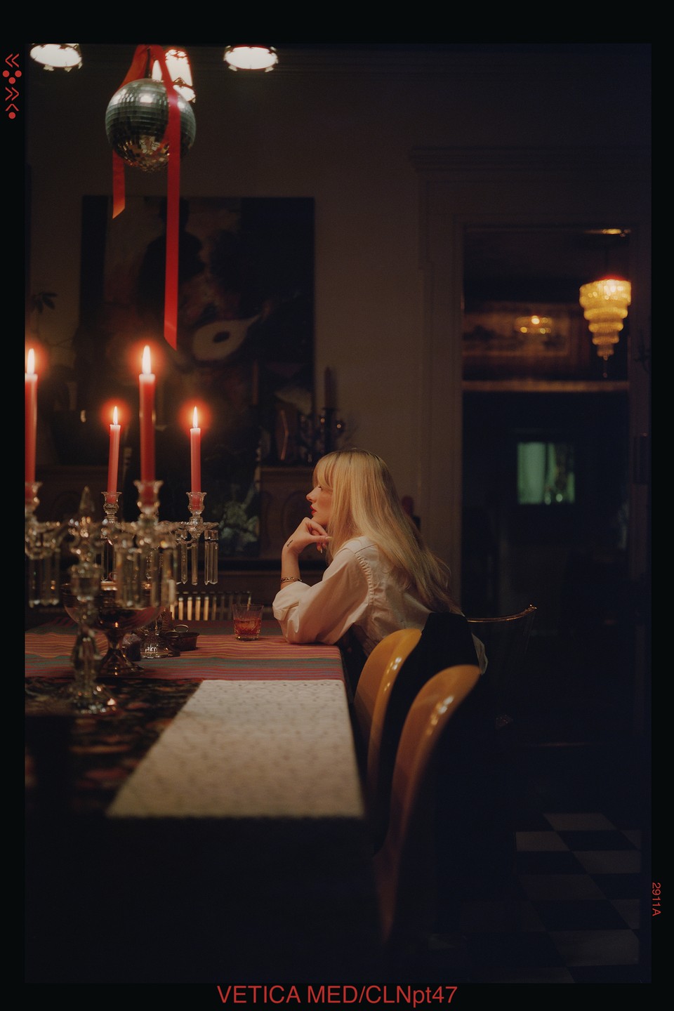A woman with long blonde hair sits at a candlelit dining table, looking to the right.