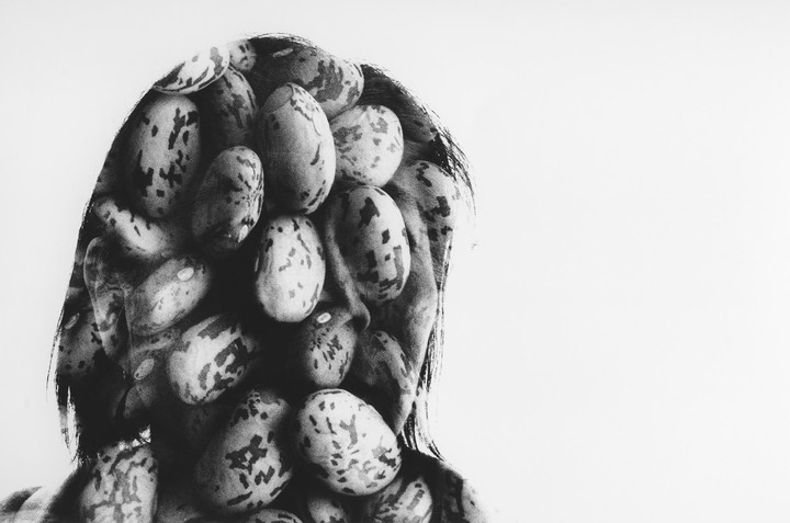 A person's face is covered with speckled beans in a surreal black and white portrait.