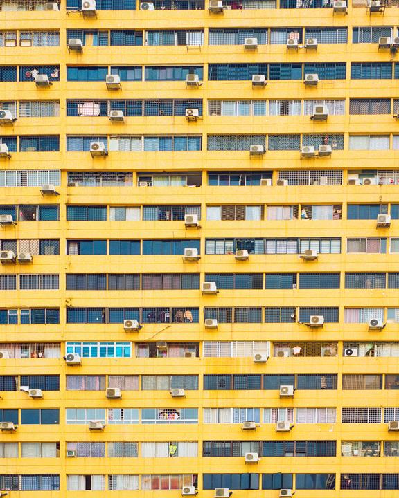 A yellow apartment building with many windows and air conditioning units is shown.