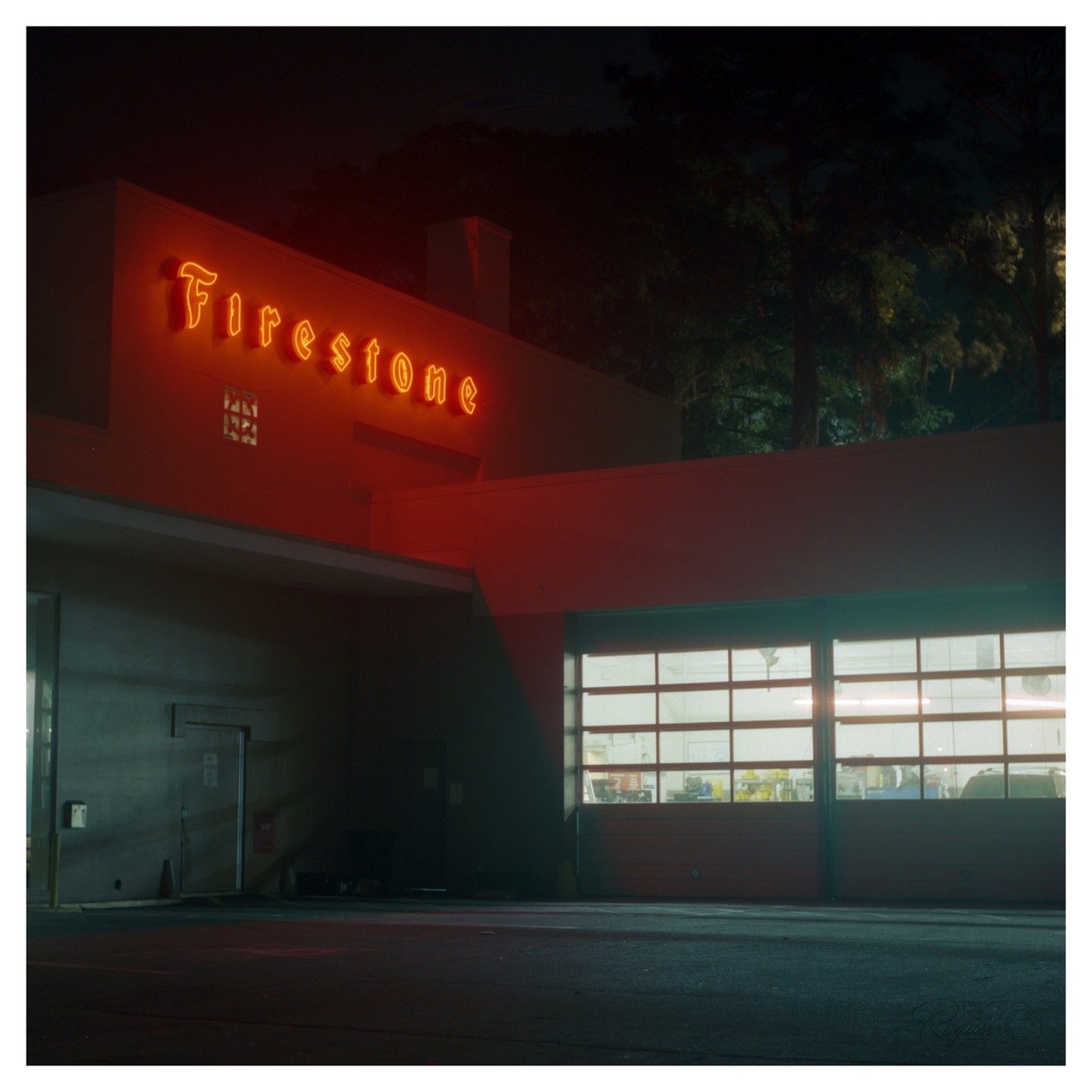 A neon "Firestone" sign glows red above a garage door with illuminated windows at night.