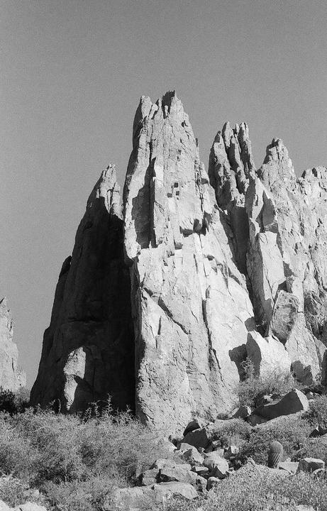 Jagged rock formations rise from a desert landscape under a clear sky.