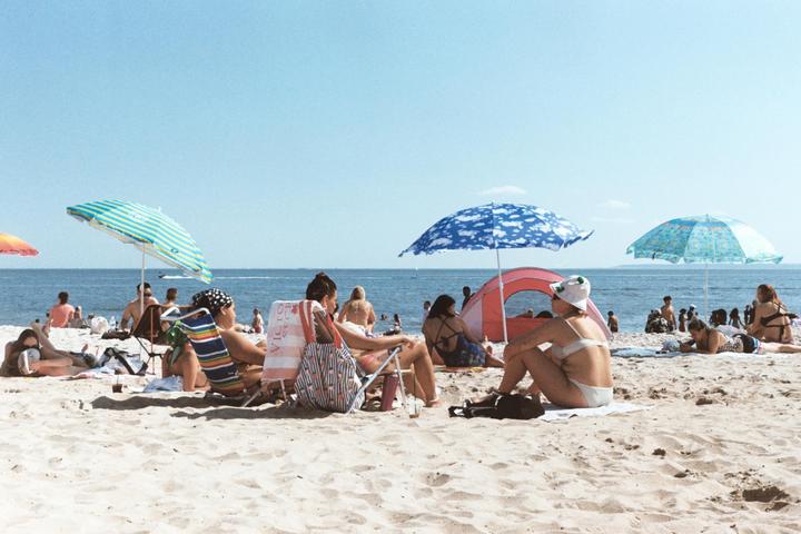 People relax on a sandy beach with umbrellas and the ocean in the background.