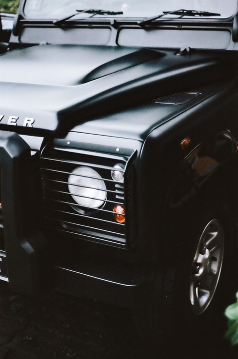 A black Land Rover is parked with its front grille and headlight visible.