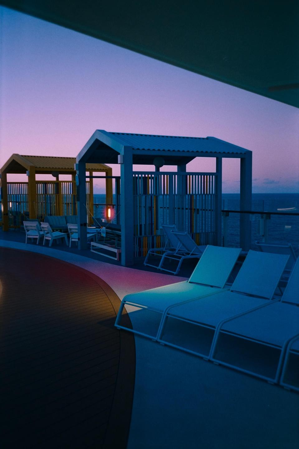 A deck with lounge chairs and cabanas overlooks the ocean at dusk.