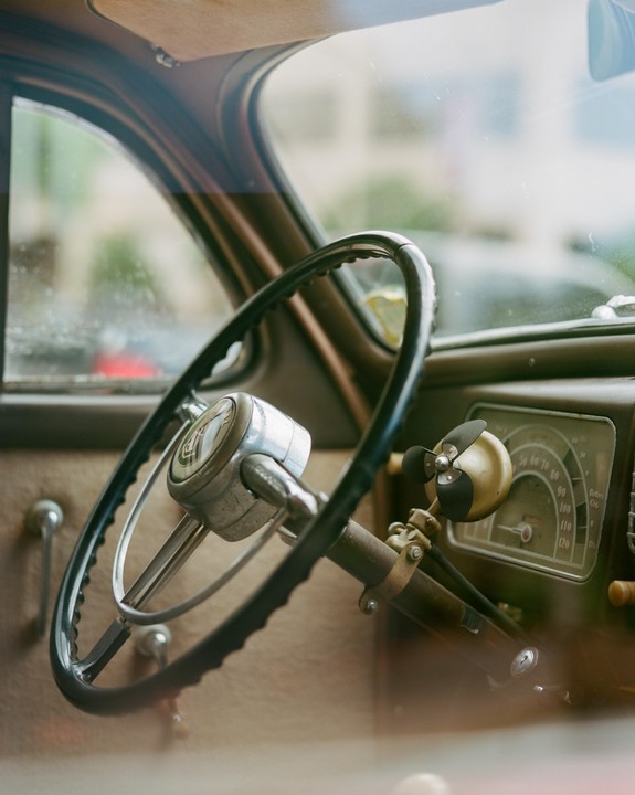 A close-up view of the interior of a vintage car shows the steering wheel and dashboard.