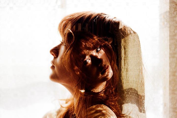 A woman with red hair is shown in a double exposure with one profile and one face looking forward.