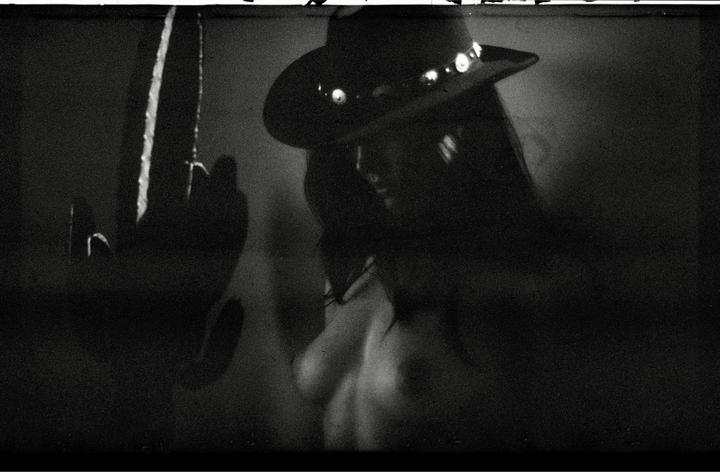 A woman wearing a hat is visible in a dark, grainy, black and white portrait.