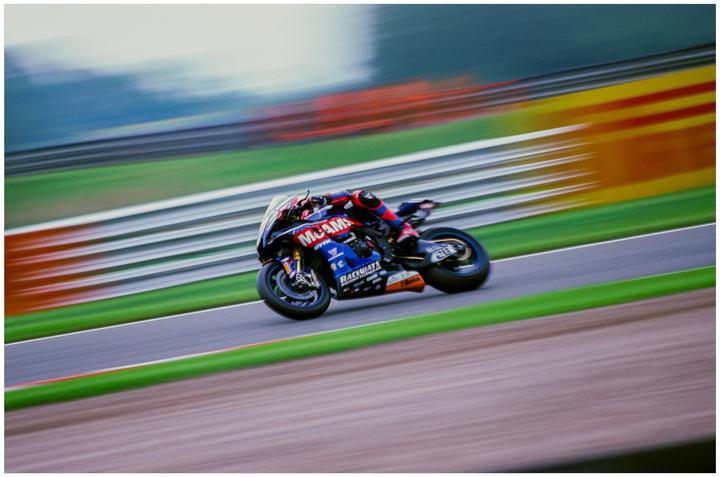 A motorcycle racer leans into a turn on a track with motion blur in the background.