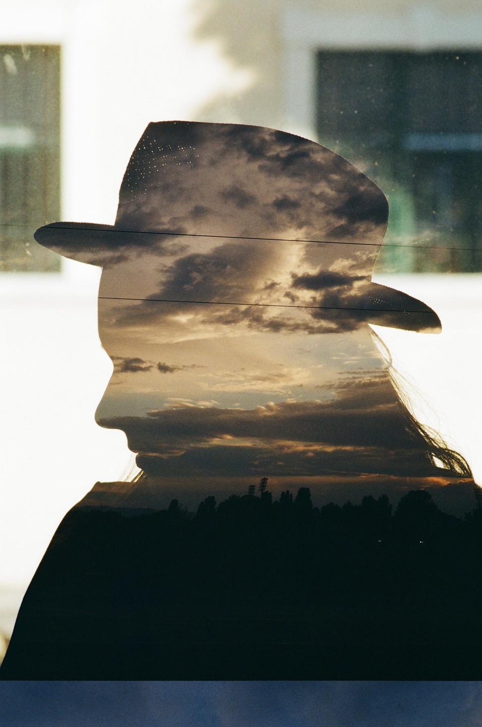 A double exposure shows the silhouette of a woman in a hat overlaid with a cloudy sunset sky and a dark landscape.