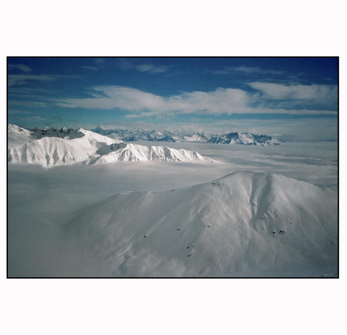 A vast mountain range covered in snow is visible above a sea of clouds under a blue sky.