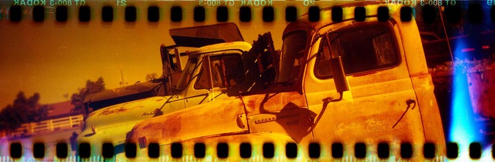 Three old, rusty trucks are parked in a row under an orange sky, with a bright blue light streak on the right.