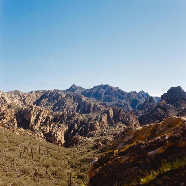 A vast desert landscape features rugged mountains under a clear sky, with cacti and shrubs populating the foreground.