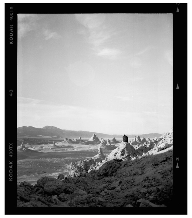 A person sits on a rock formation overlooking a desert landscape with many tufa towers and mountains in the distance.