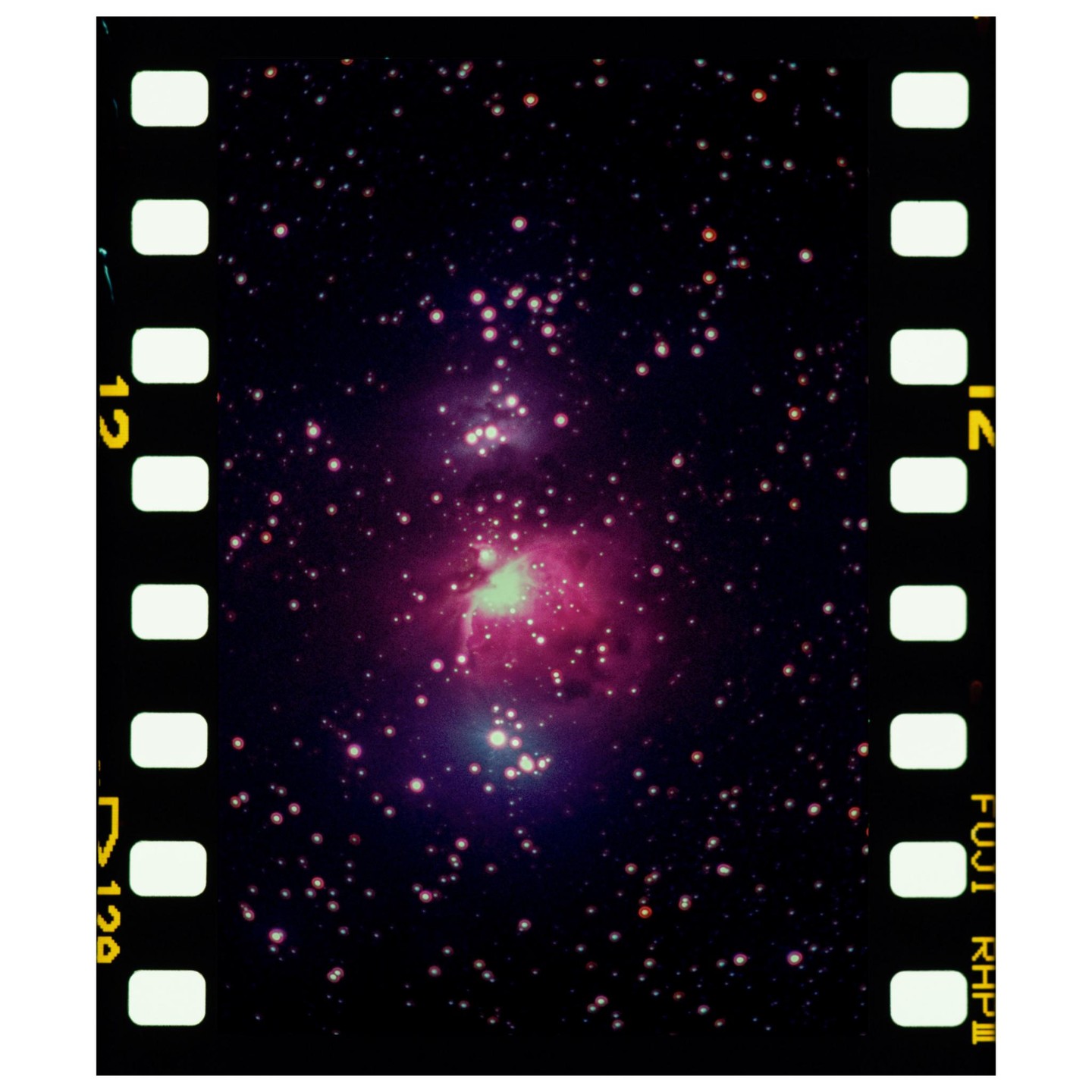 A nebula with pink and green hues is surrounded by numerous stars, framed by the sprocket holes of a film strip.