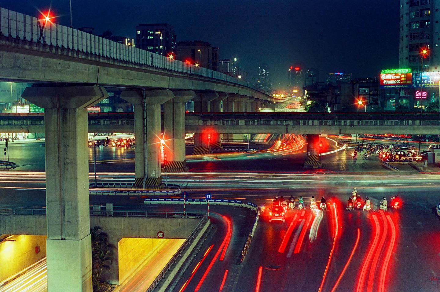 A busy city intersection at night is illuminated by the light trails of vehicles and streetlights.