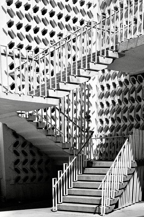 A multi-level outdoor staircase with white railings is set against a patterned wall.