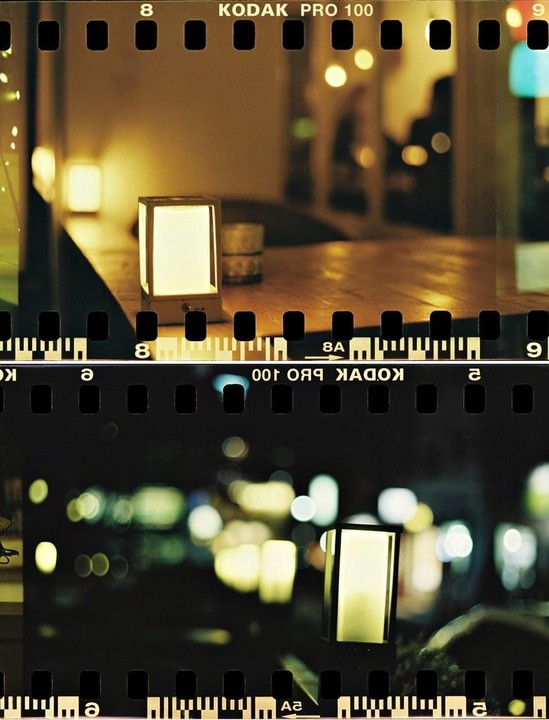 Two glowing rectangular lamps are visible, one on a wooden table and another in a dark, blurry setting with bokeh lights.