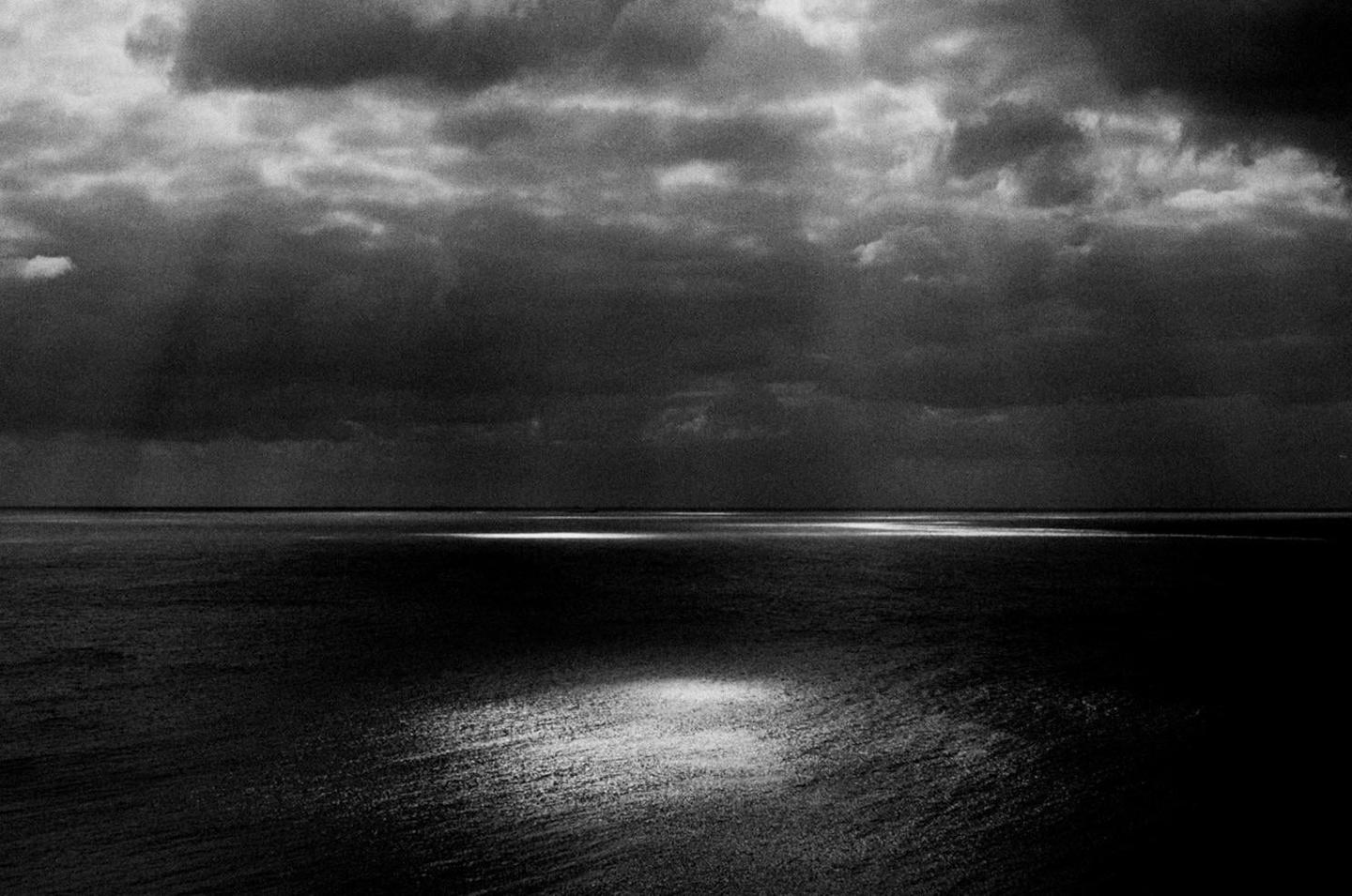 Sunlight breaks through dark clouds and illuminates the surface of a body of water.